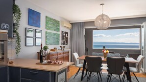 A modern kitchen with a dining area, featuring a large window with a view of the sea, a chandelier, and various artworks on the walls. - Sun Spalato Art (Split)