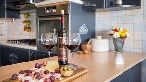 A kitchen counter with a bottle of wine, two glasses, and a cheese board with grapes and olives. - Sun Spalato Art (Split)