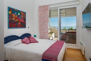 A bedroom with a bed, a colorful painting, a patterned curtain, and a view through a sliding glass door. - Sun Splato Space (Split)