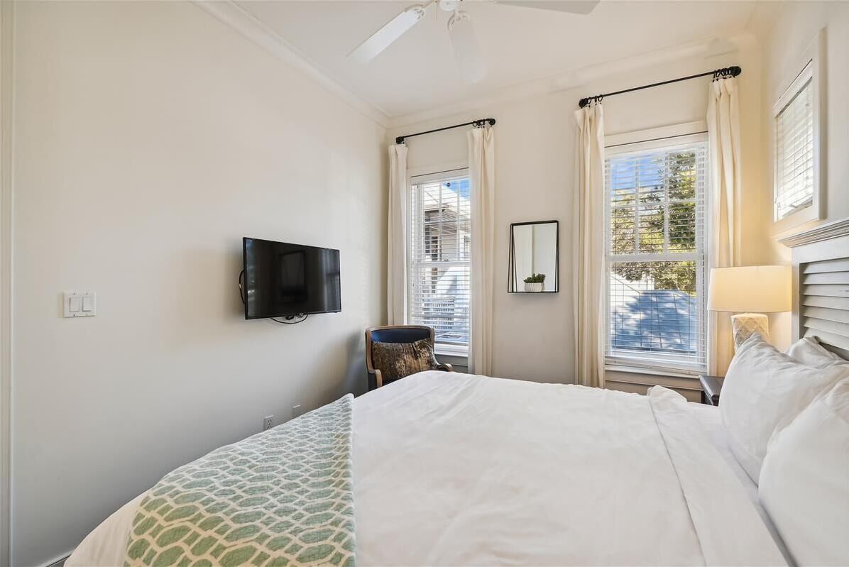 A hotel room with a bed, a television mounted on the wall, a window with curtains, and a small table with a chair.