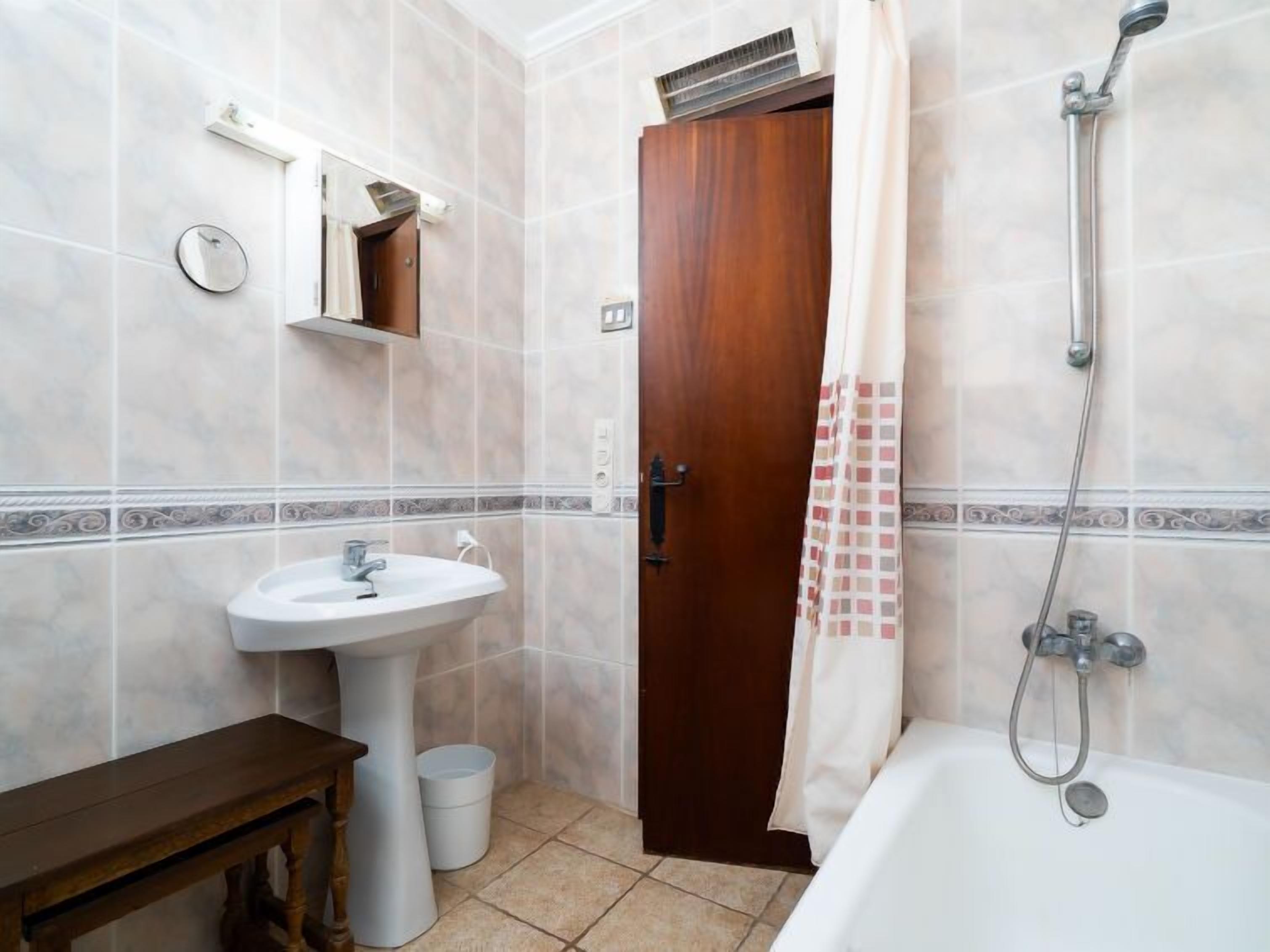 A bathroom with a sink, a wooden bench, a door, and a shower.