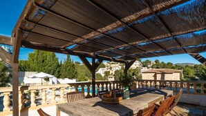 An outdoor patio with a wooden table and chairs, a pergola overhead, and a view of a pool and buildings in the background. - Sunshine by Interhome (Moraira)