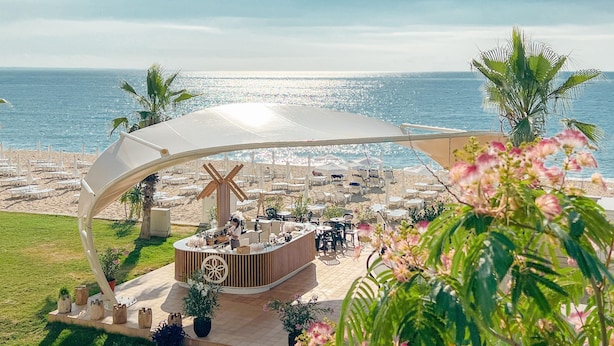 Un bar situé en bord de mer, doté d’un auvent incurvé, de places assises en plein air et d’une vue sur l’océan.