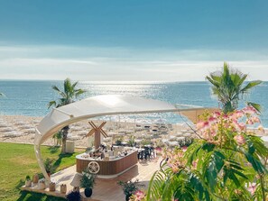 Eine Strandbar mit gewölbtem Dach, Sitzgelegenheiten im Freien und Blick auf das Meer.