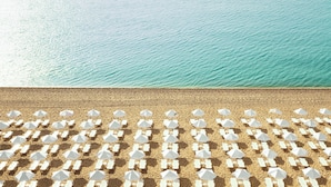 Une plage bordée de rangées de chaises longues et de parasols blancs, offrant une vue dégagée sur la mer turquoise.