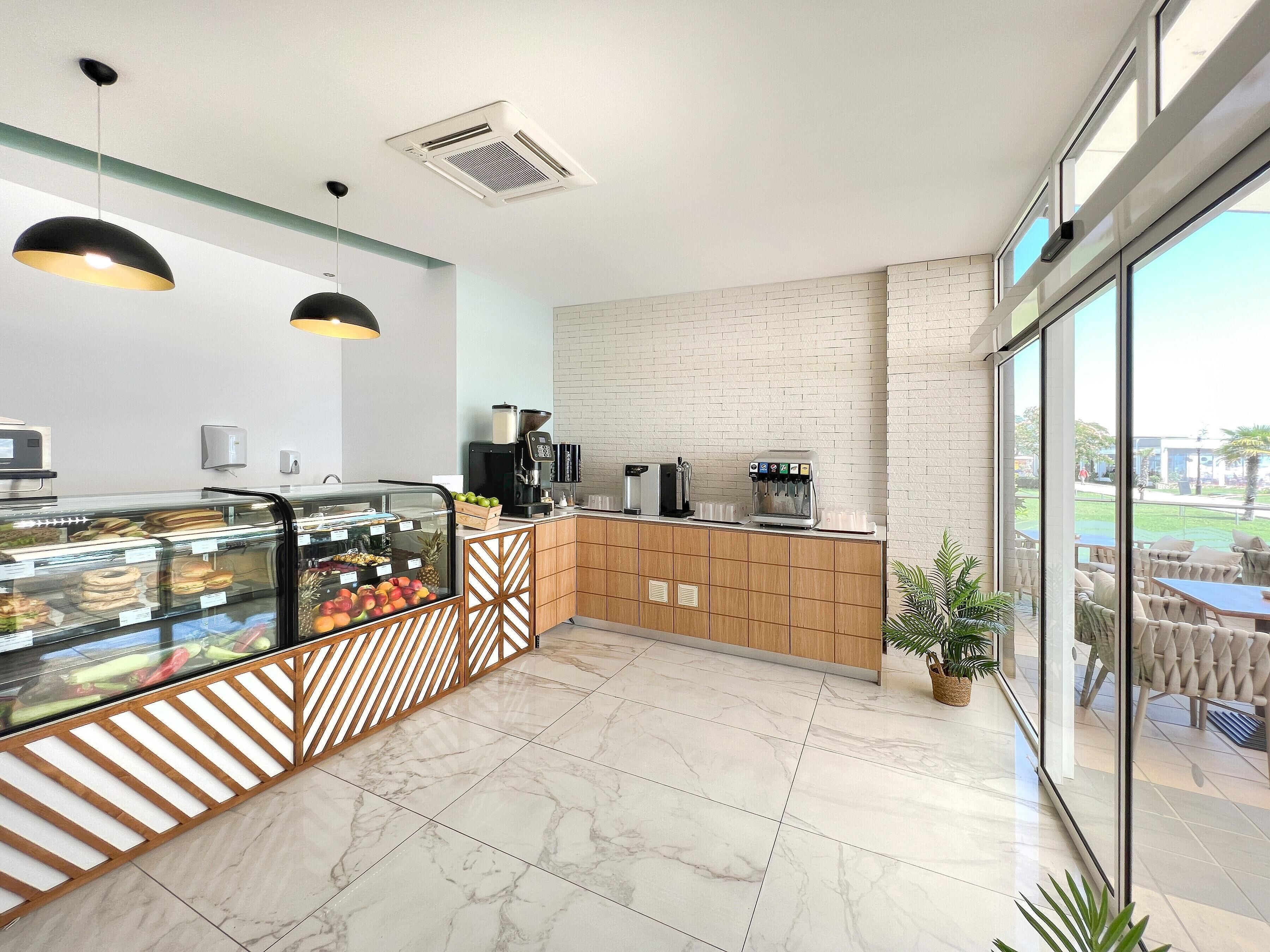 Een modern café met een marmeren vloer, een glazen vitrine met gebak, een koffiemachine en een zitgedeelte met uitzicht.