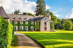 Un grand bâtiment en pierre, doté d’une façade symétrique, d’une entrée centrale et d’une pelouse bien entretenue.