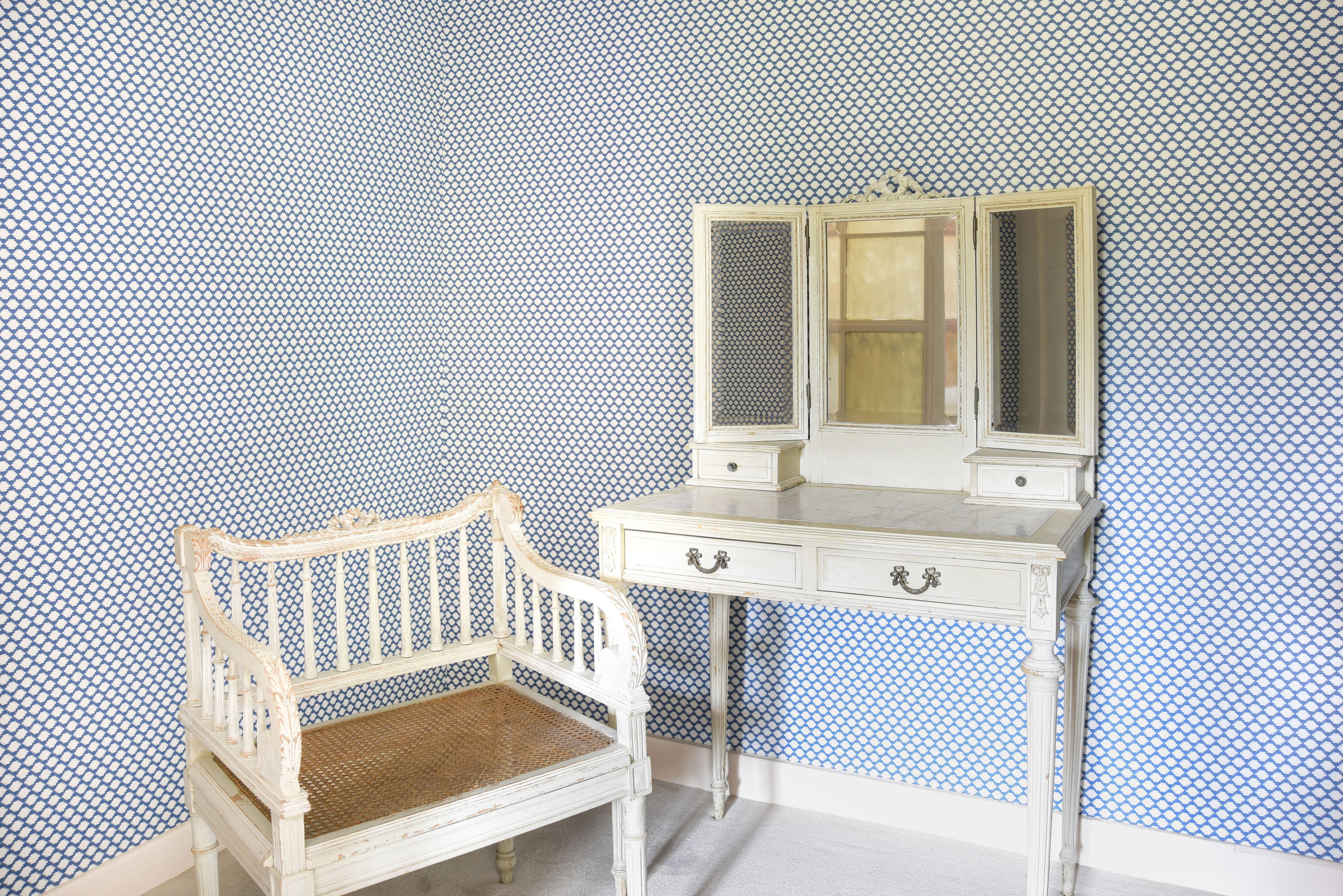 Una cómoda blanca con espejo y una silla frente a una pared con estampado.