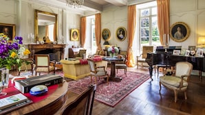A room with a fireplace, a piano, and a dining area with a red rug. - Château de la Villedubois (Mordelles)