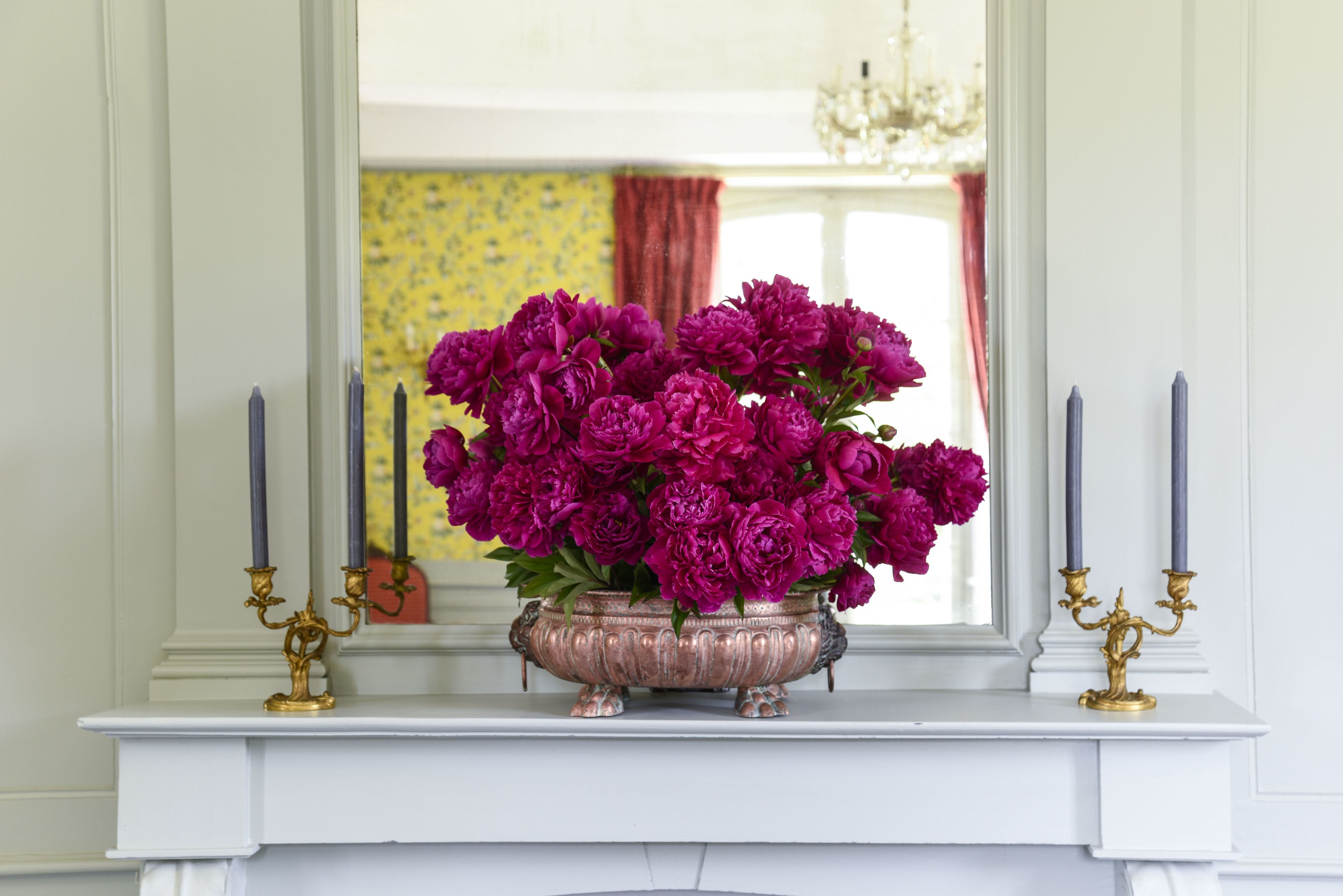 A white fireplace mantel with a decorative metal vase holding purple flowers and two candle holders.