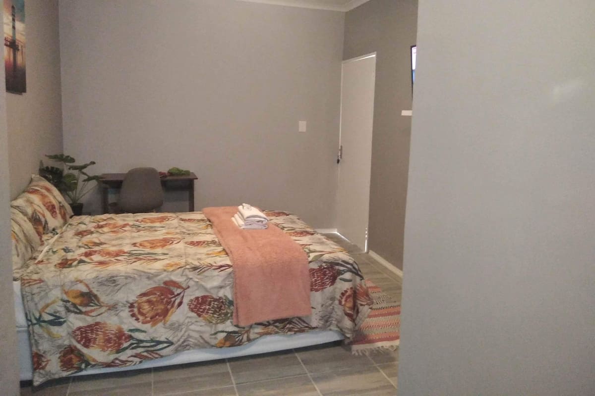 Un dormitorio con cama, una silla, una mesita y una planta.