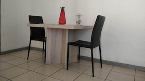 Een klein zitehoekje met een houten tafel en twee zwarte stoelen. Op de tafel staat een rode vaas met een plant.