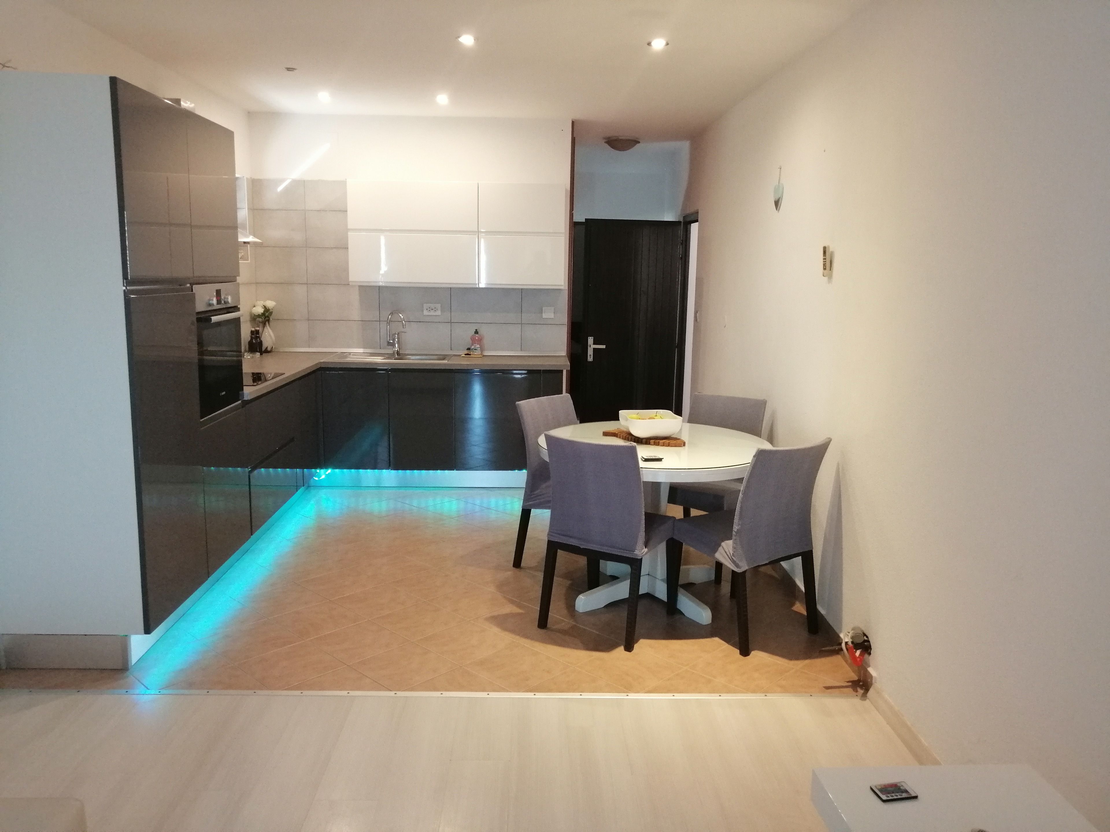 A modern kitchen with dark cabinets, a white countertop, and a round dining table with four chairs.