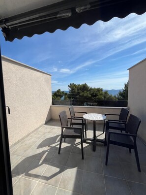 A covered outdoor seating area with a table and chairs, a view of the sea, and a building with a textured wall. - Hotel Ana Murter (Murter-Kornati)
