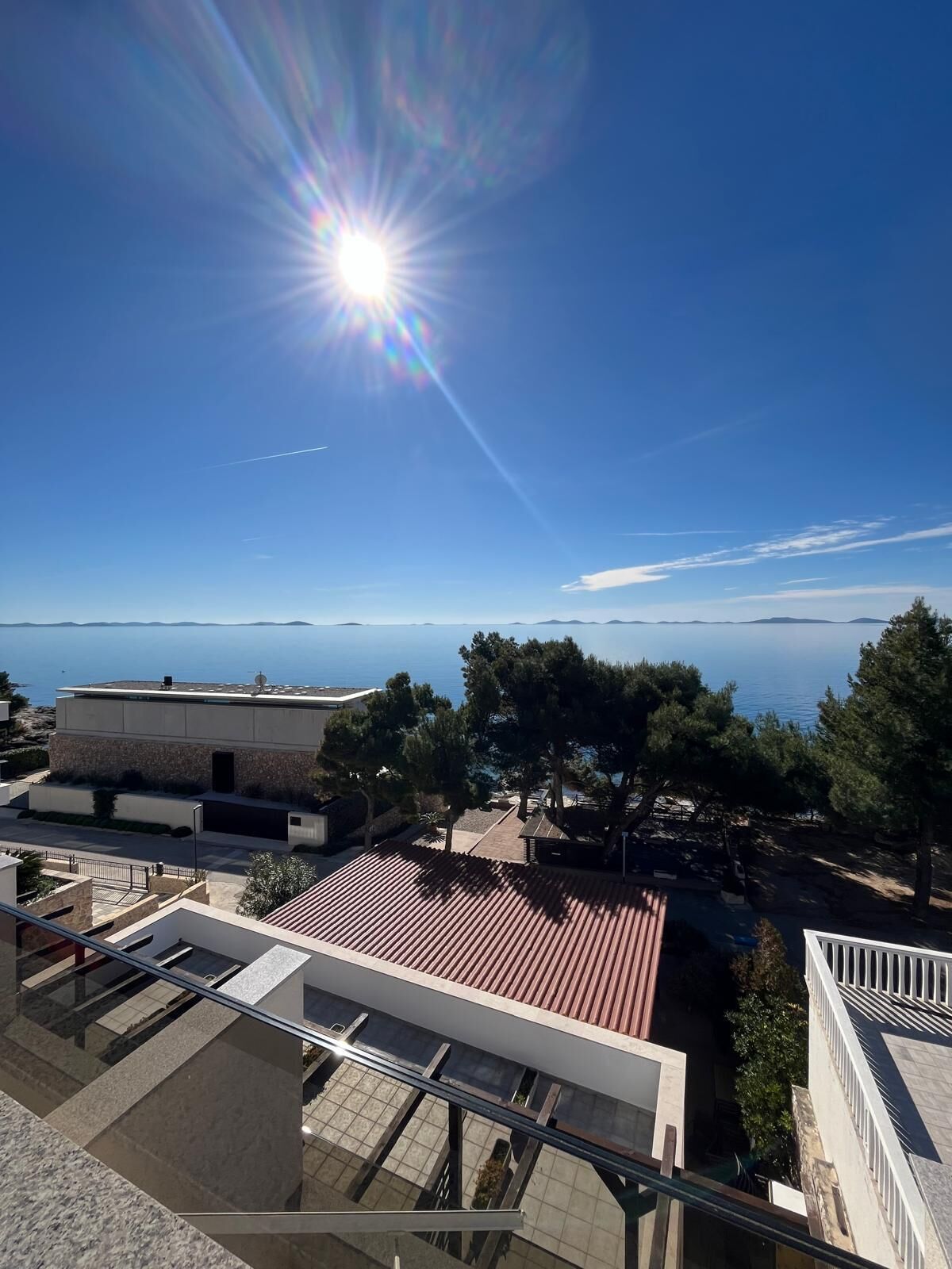 A modern building with a red-tiled roof, a glass balcony, and a view of the sea and distant islands.