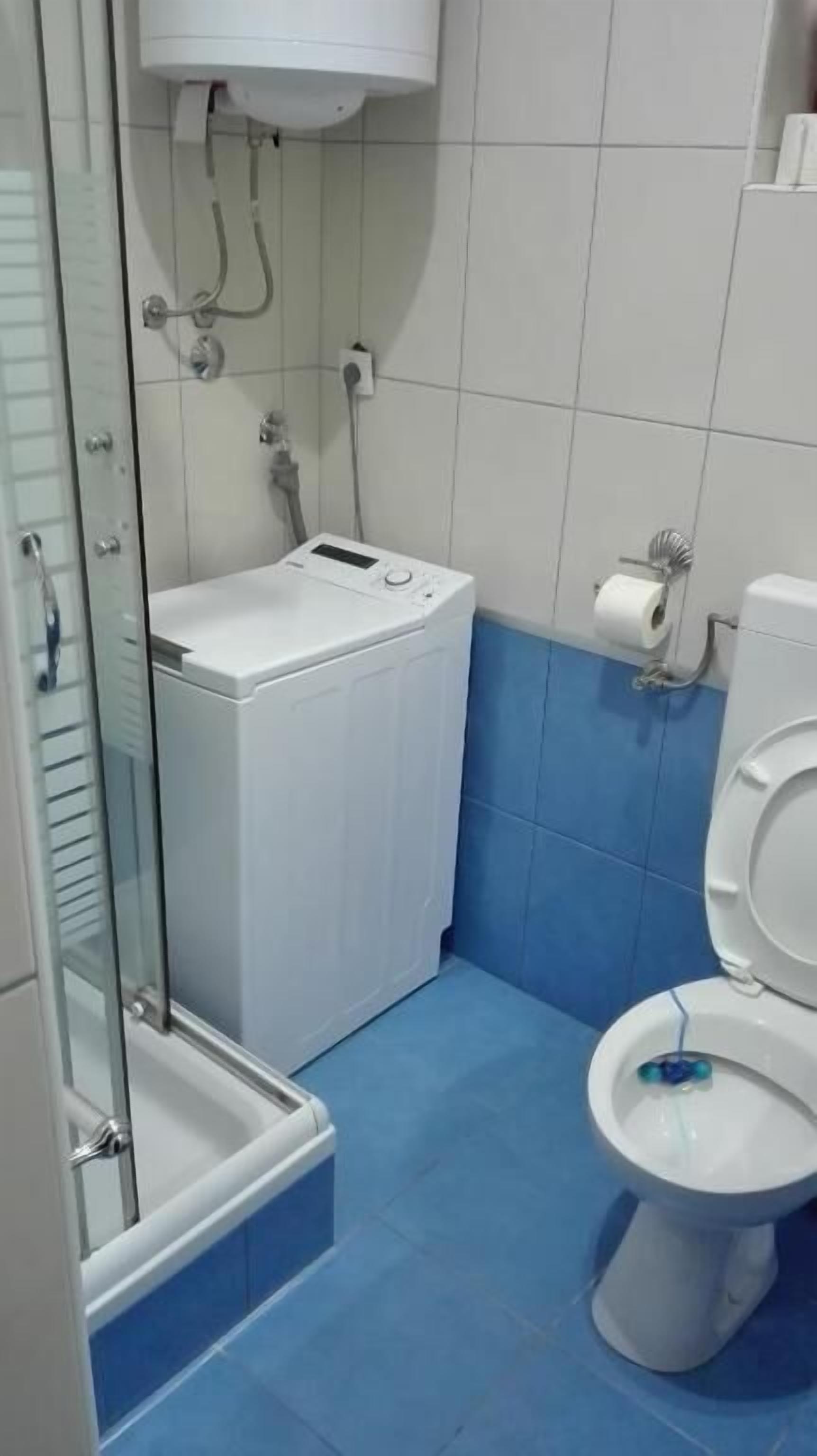 Un baño con ducha, inodoro y lavadora.