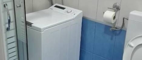 Un baño con ducha, inodoro y lavadora.