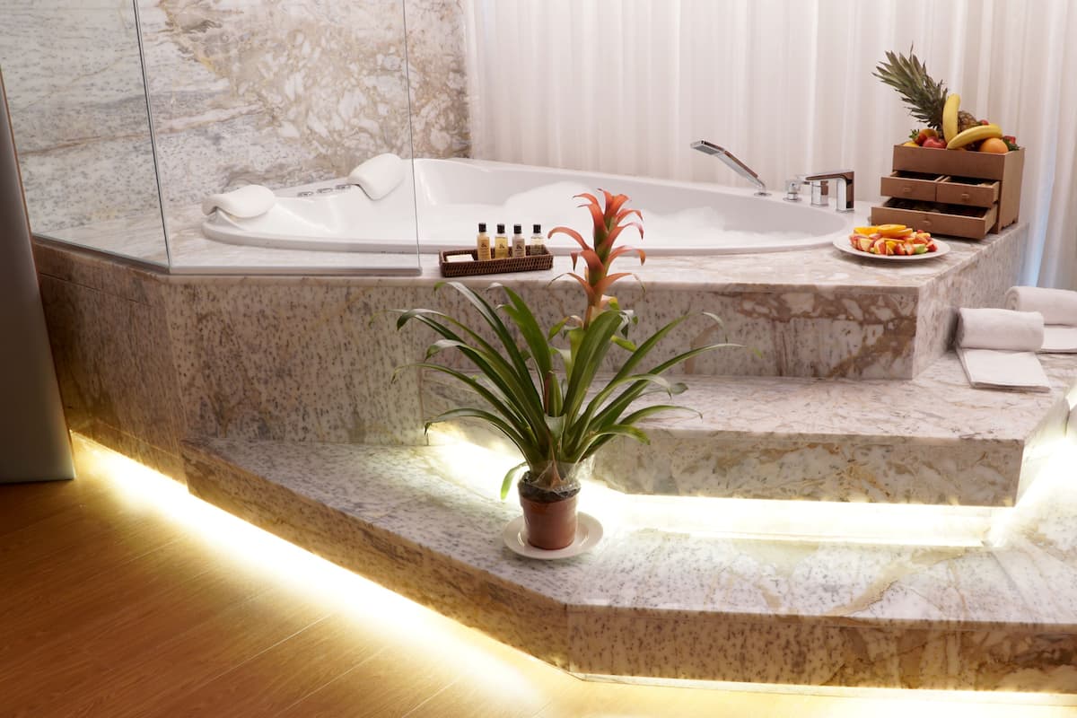 A modern bathroom with a marble sink, a bathtub, a potted plant, a fruit basket, and neatly folded towels.