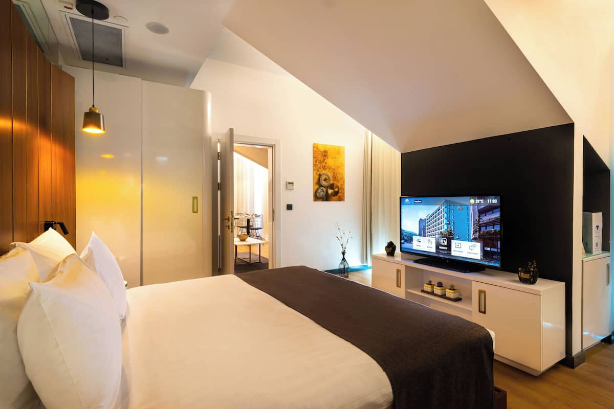 A modern hotel room with a large bed, a flat-screen TV, a desk, and a wardrobe.