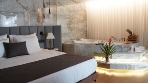 A modern hotel room with a large bed, a marble wall, a bathroom with a bathtub, and a fruit basket. - The Craton Hotel (Istanbul)