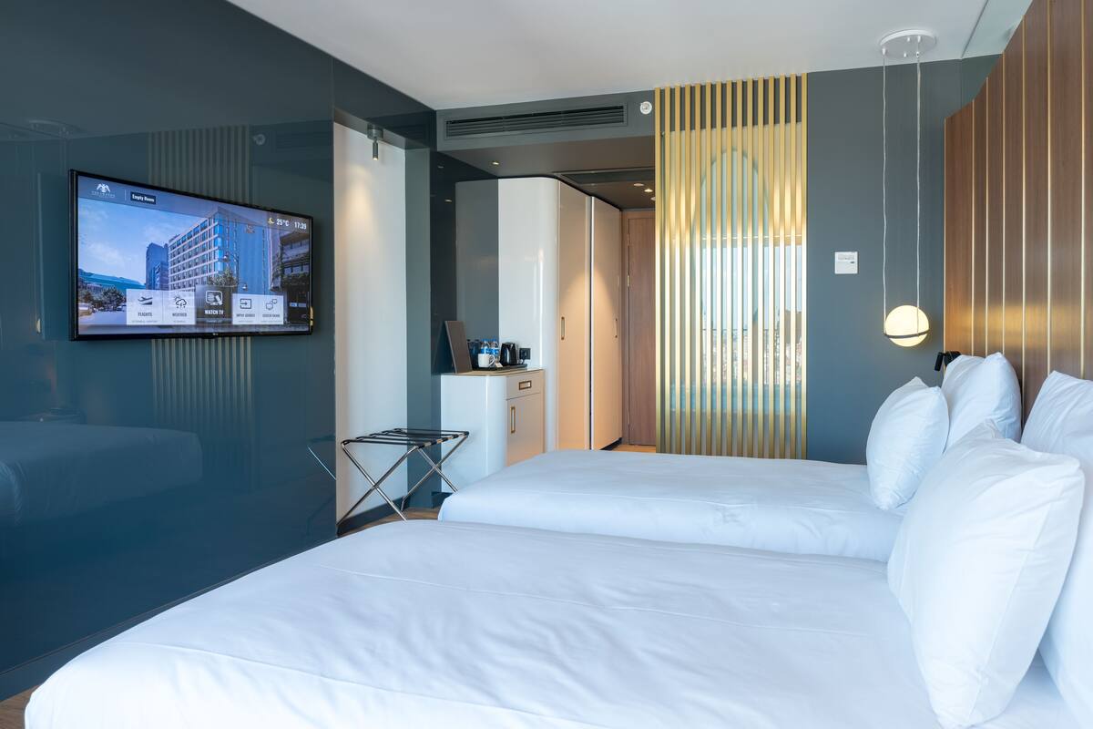 A modern hotel room with a large bed, a TV mounted on the wall, and a small table with a kettle and cups.