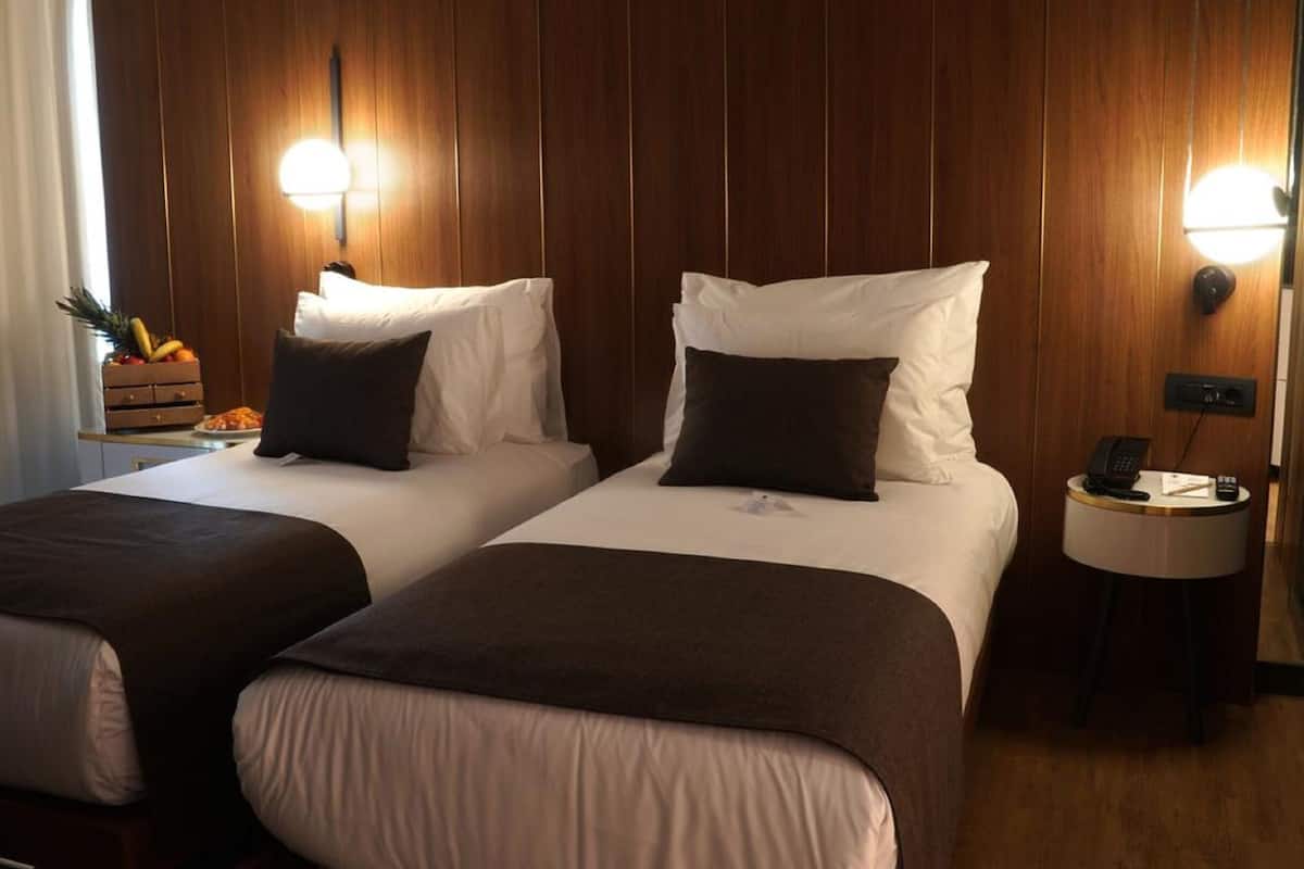 A hotel room with two beds, wooden paneling, and bedside lamps.