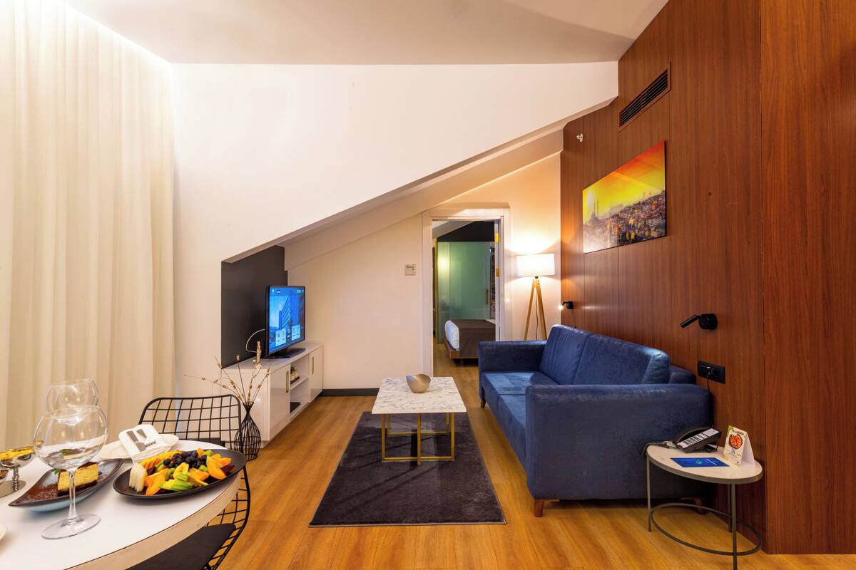 A modern living room with a sofa, a coffee table, a TV, and a dining area with a table set for two.