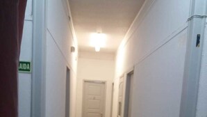 A narrow, well-lit hallway with a tiled floor, white walls, and a closed door at the end. - Ayurvida (Barreiro)