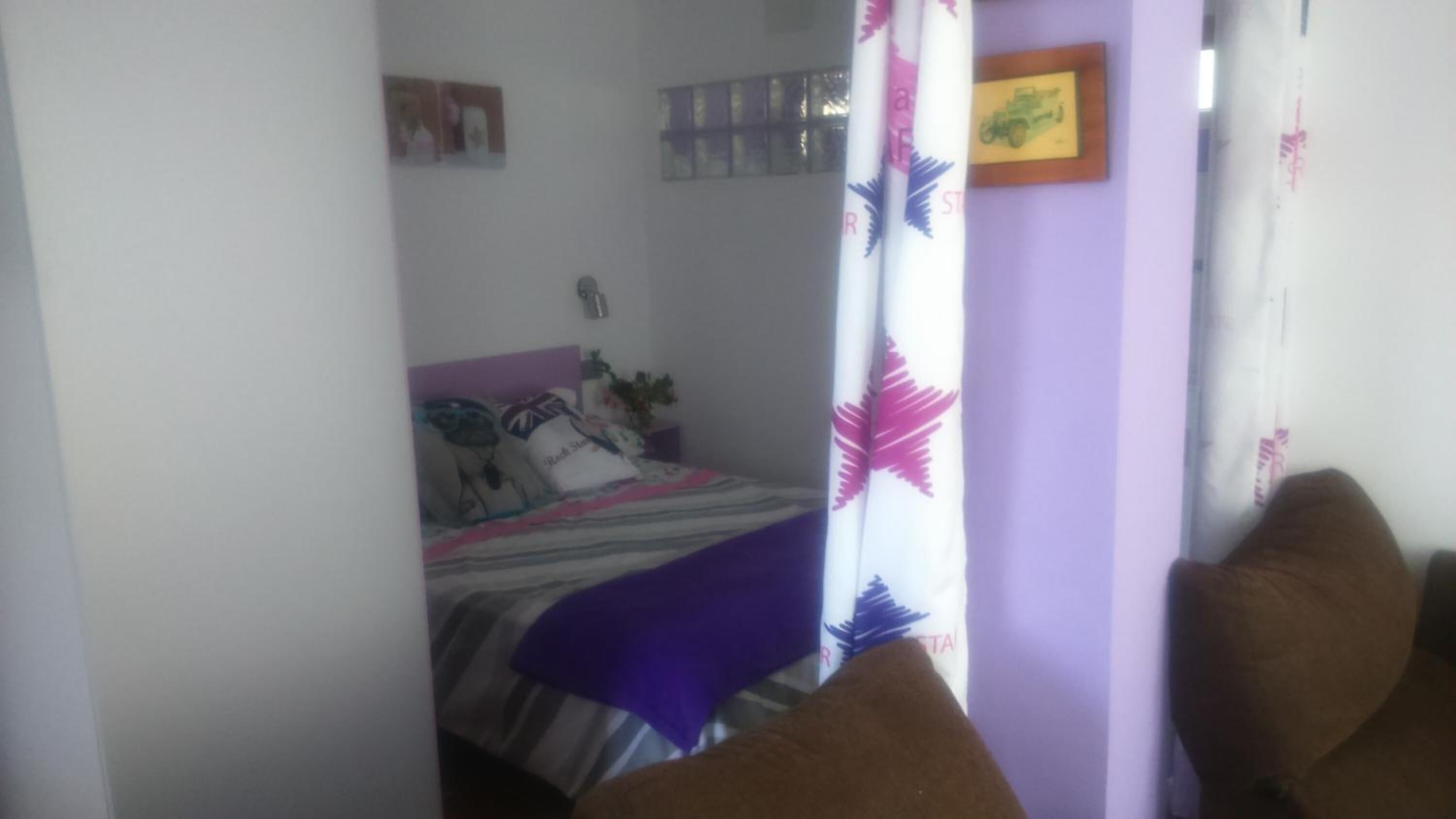 Une chambre à coucher avec un lit, une table de chevet, une plante et une étagère fixée au mur.
