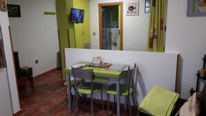 Un pequeño comedor con una mesa y sillas, un televisor montado en la pared, y una puerta que da a otra habitación.
