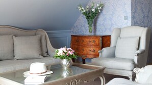 Una habitación con papel tapiz estampado, un sofá, una silla, una mesa de centro con un jarrón de flores y un mueble de madera.