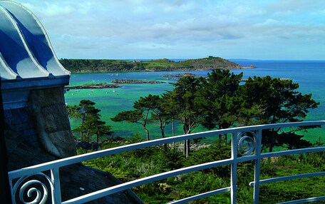 A coastal view with a stone structure, a metal railing, and a clear blue sea.