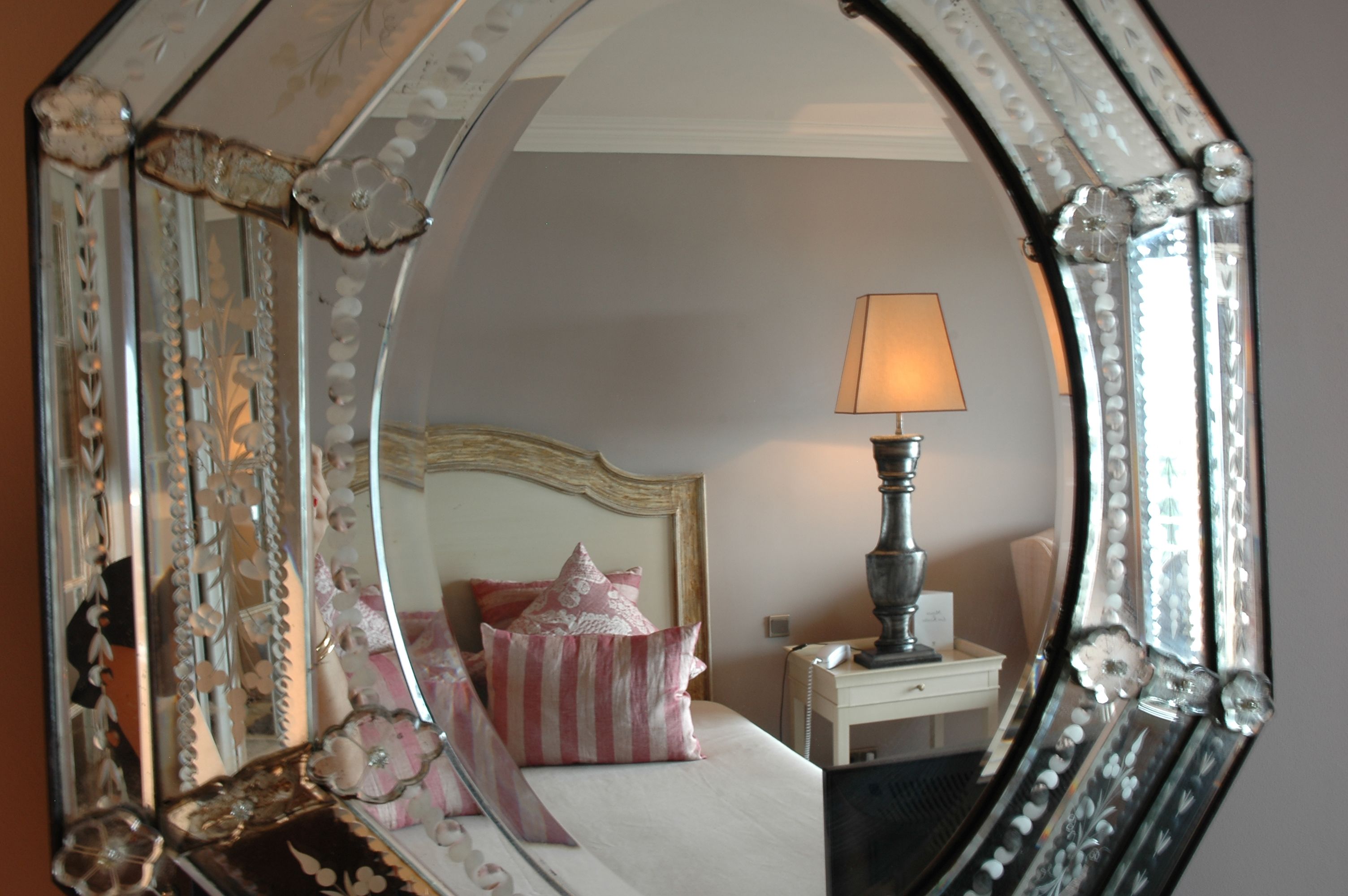 Une chambre à coucher comprenant un lit, des oreillers, une table de chevet, une lampe et un miroir aux motifs décoratifs.