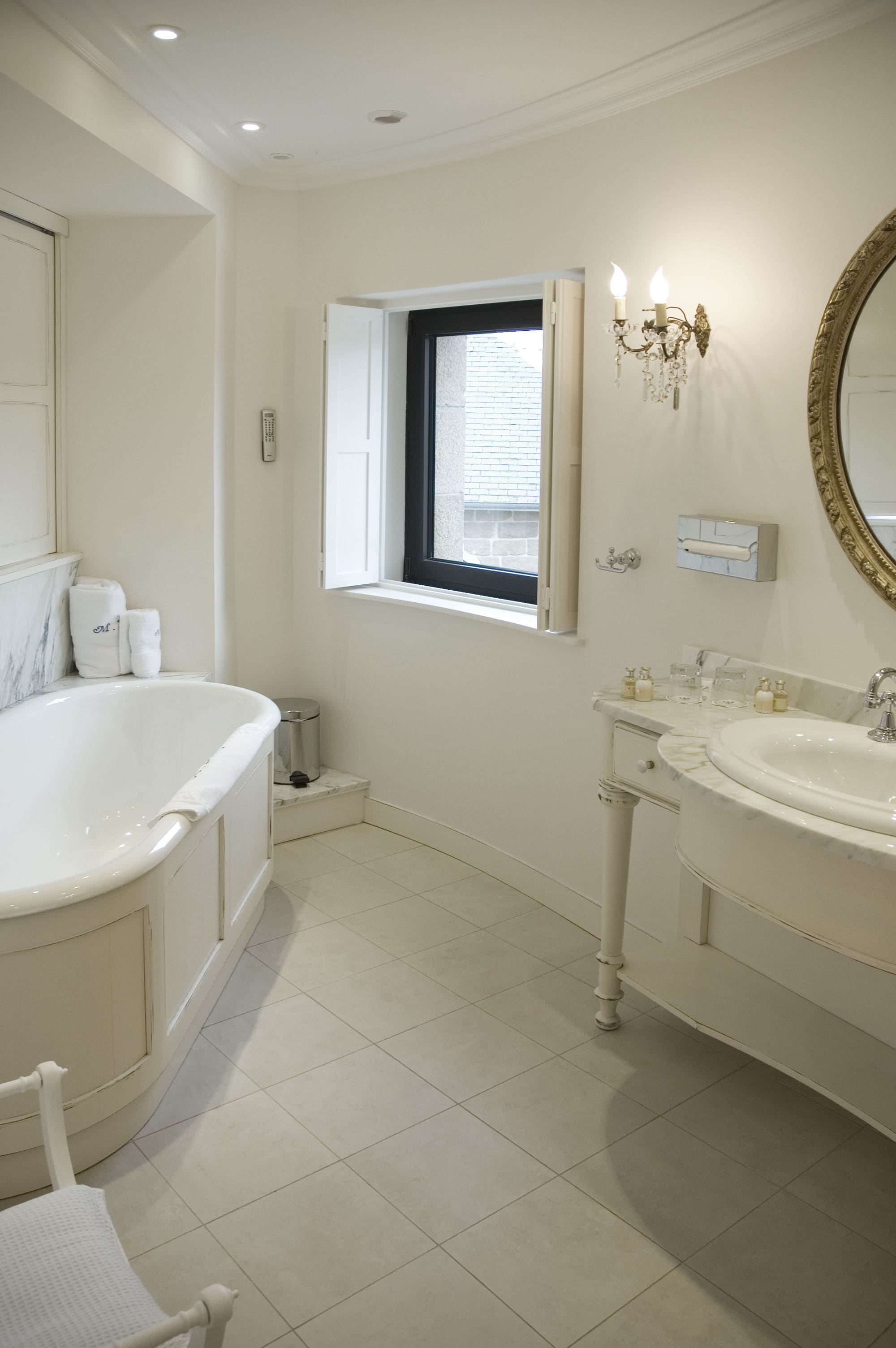 Un baño con bañera, lavamanos, tocador, espejo y ventana con persianas.