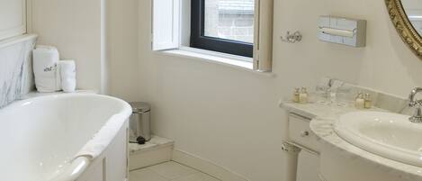 Un baño con bañera, lavamanos, tocador, espejo y ventana con persianas.