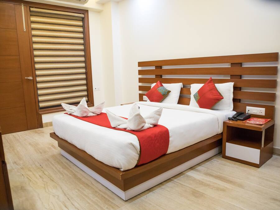 Una cama bien hecha con ropa de cama blanca y roja, un cabecero de madera y una mesita de noche con un teléfono y un libro.