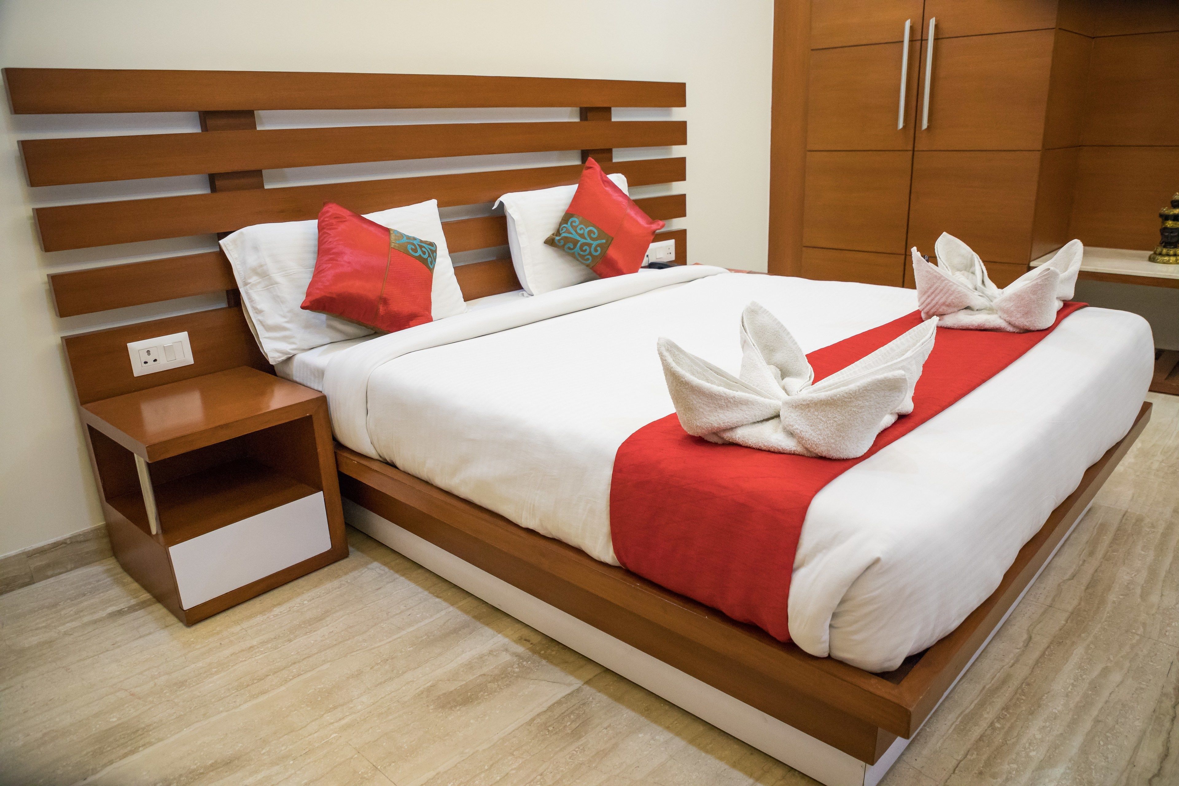 A neatly made bed with white and red bedding, wooden headboard, and matching nightstand.