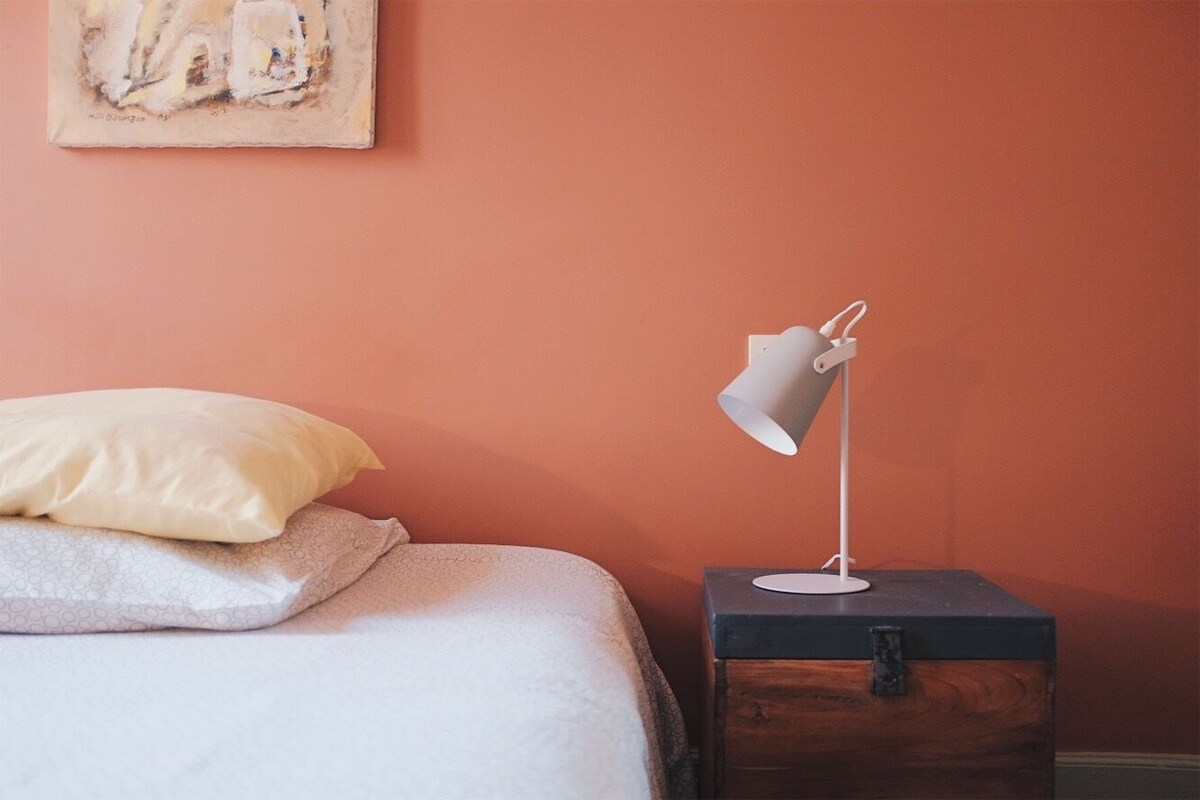 A neatly made bed with pillows, a bedside table with a lamp, and a painting on the wall.