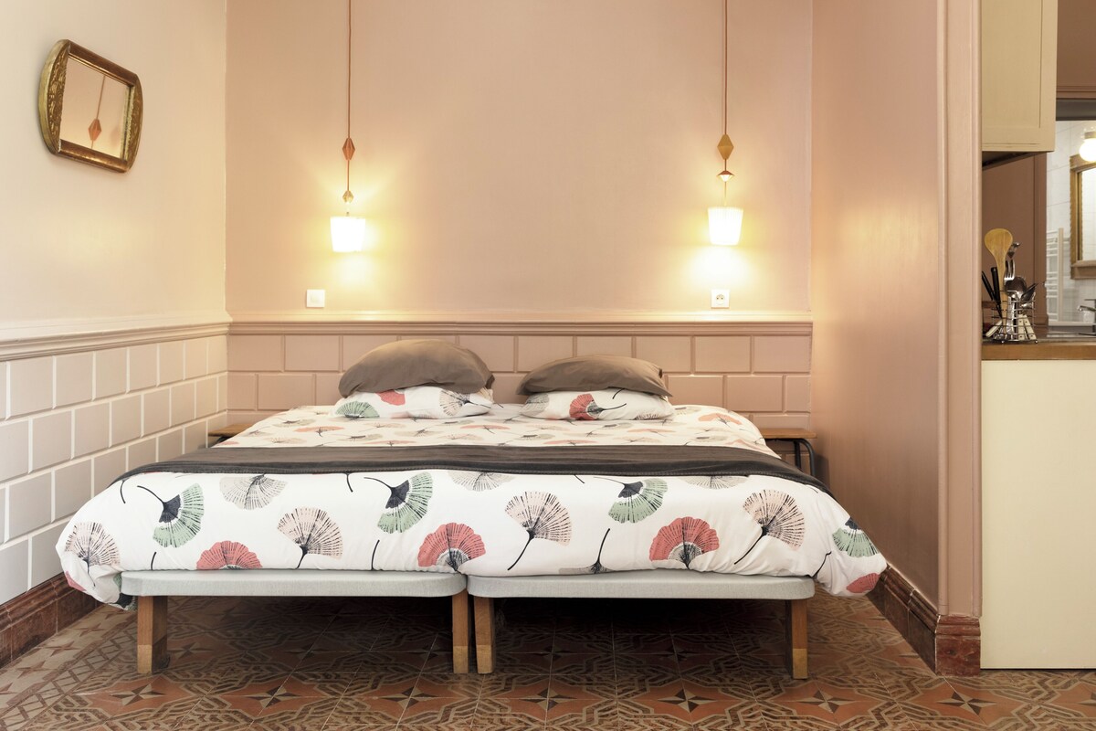 A double bed with a floral bedspread, two bedside lamps, and a small bedside table with a mirror and toiletries.