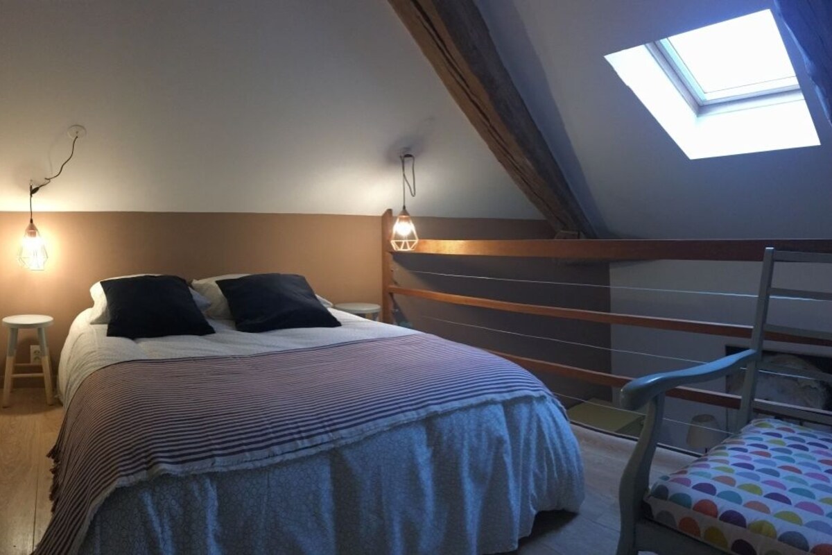 A bedroom with a bunk bed, a small stool, a chair with a colorful cushion, and a skylight.