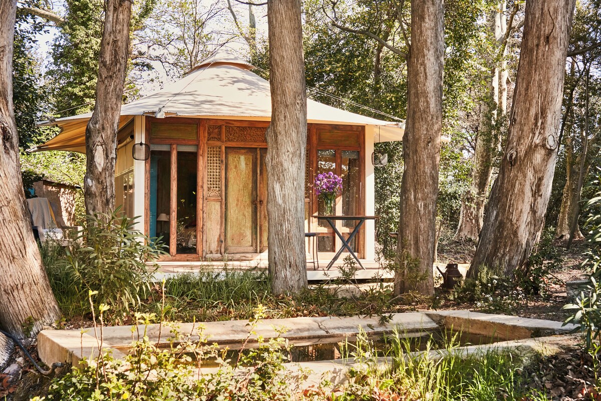 A wooden cabin with a porch, surrounded by trees.