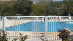 Piscina cercada por cadeiras de descanso e palmeiras, com grade de metal.