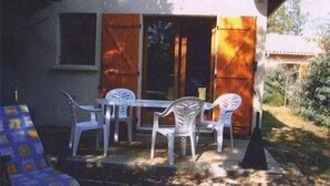 A patio with a table and four chairs, a blue patterned chair, and a wooden door. - Villa 4 p family or lovers Quiet area / garden / parking fenced / Sea 950 (Vendays Montalivet)