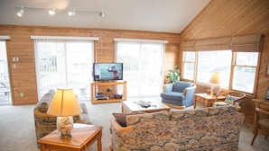 Un salón acogedor con televisor, un sillón azul, un sofá estampado y una mesa de centro de madera.