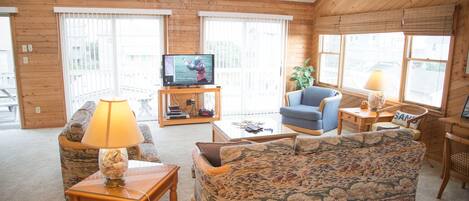 A cozy living room with a television, a blue armchair, a patterned sofa, and a wooden coffee table.