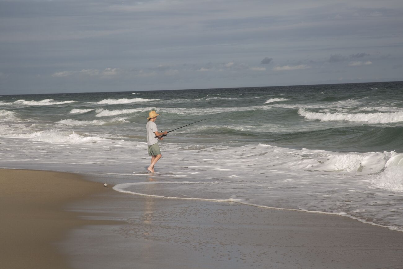 A person fishing on a beach with waves crashing onto the shore.