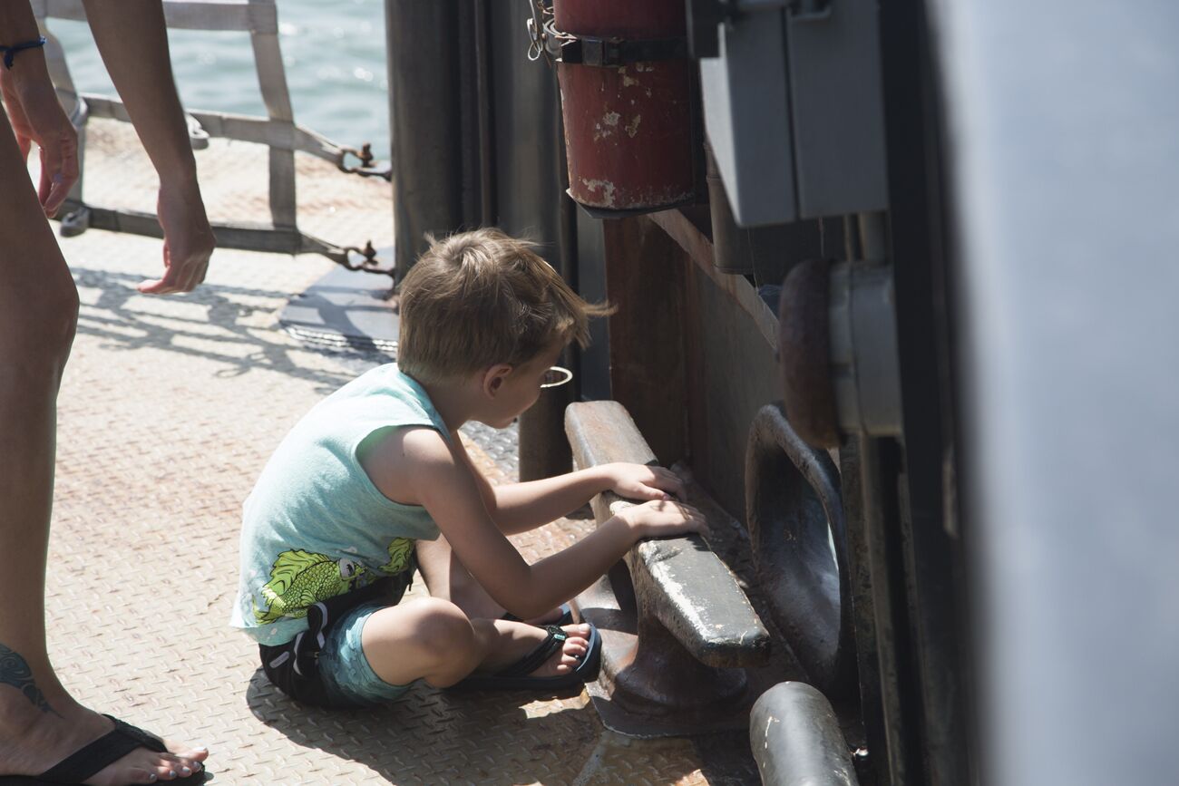 Un niño sentado en el suelo cerca de una estructura metálica, posiblemente un muelle.