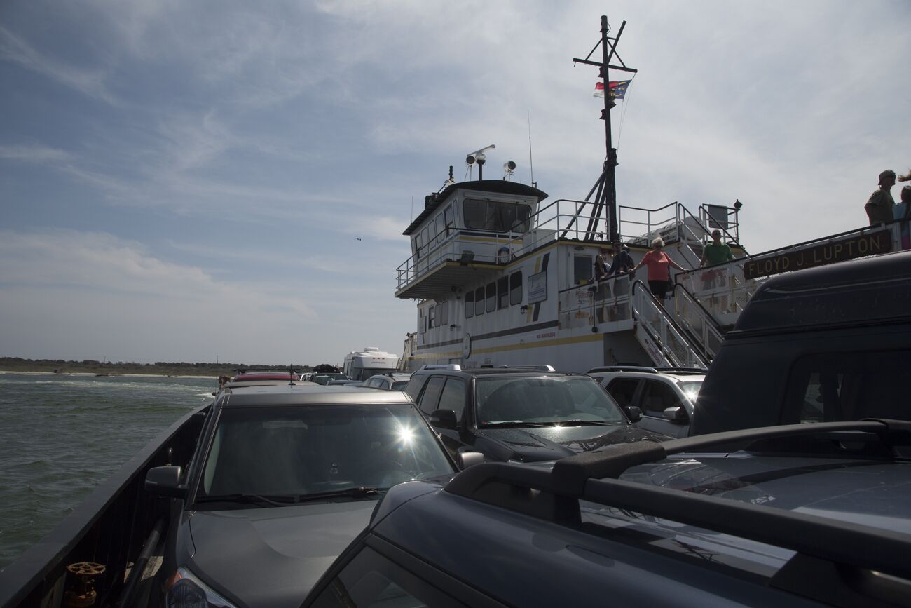 A ferry with multiple levels and a control tower, docked with cars and people nearby.