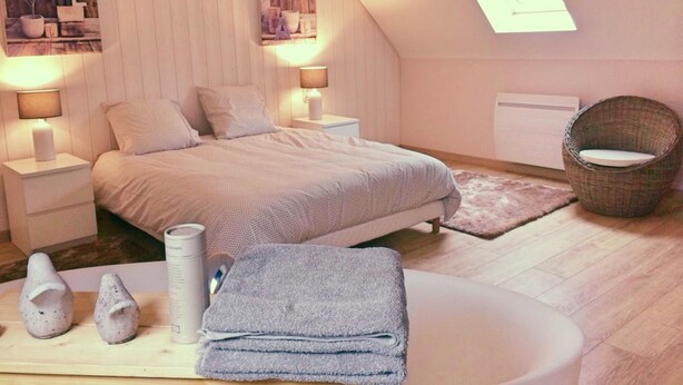 A bedroom with a bed, two bedside tables, a nightstand, a wicker chair, a small window, and a wall-mounted shelf with decorative items. - La Ferme d'Antan (Mons-Boubert)