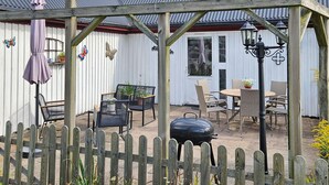 A covered patio area with outdoor furniture, a grill, and a wooden fence.